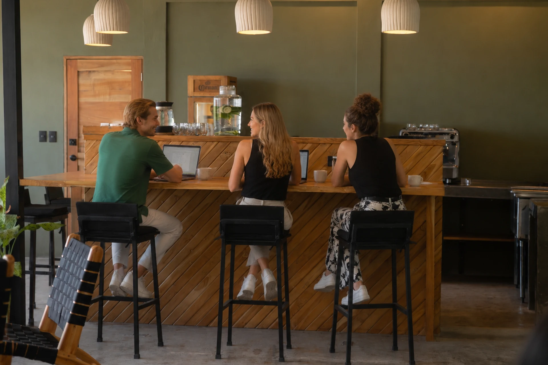 A group of remote workers and digital nomads collaborating on laptops at a wooden co-working cafe bar inside the Esc community space in Nicaragua