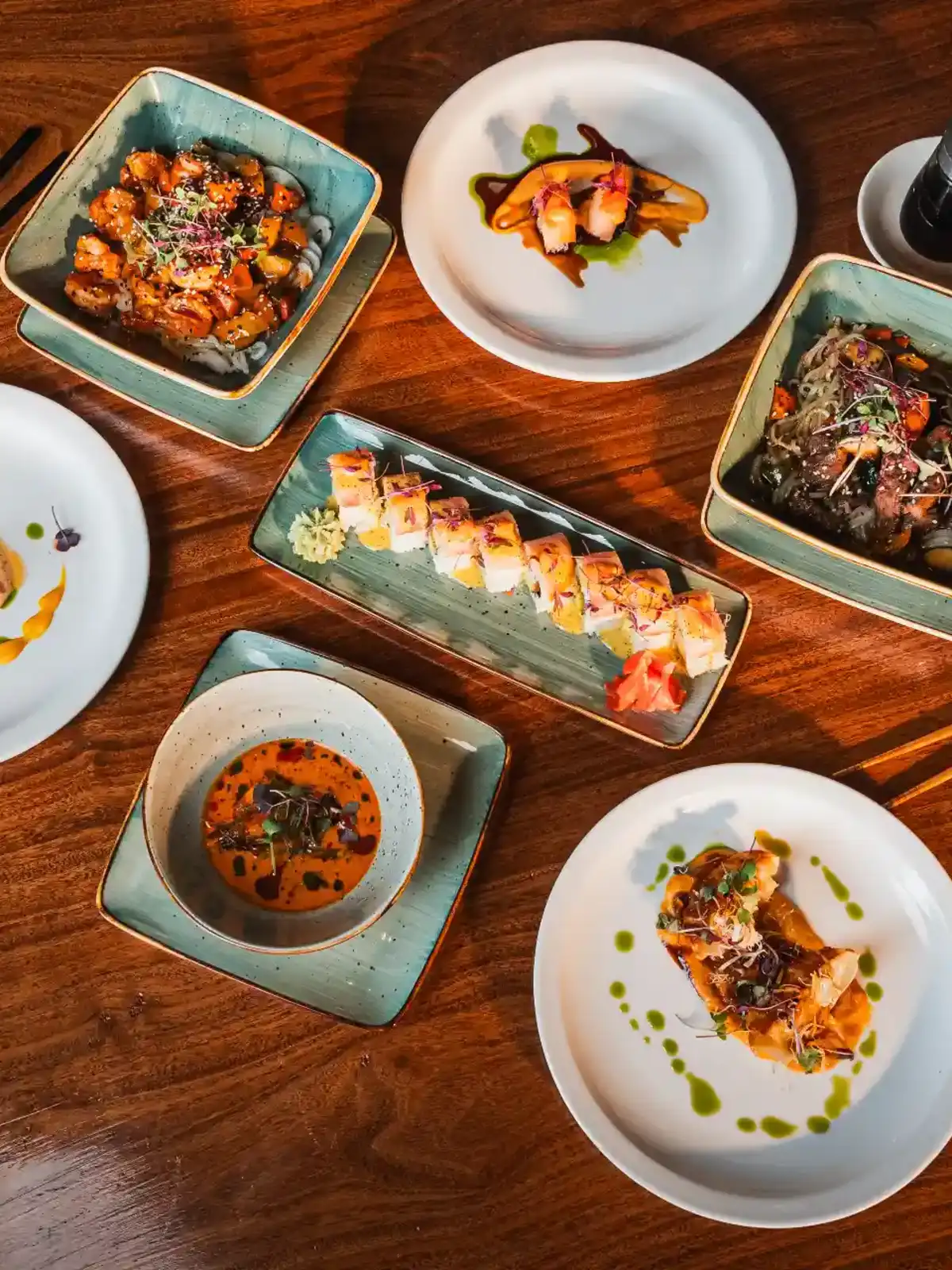 Selection of sushi and plated dishes arranged on a wooden lunch table