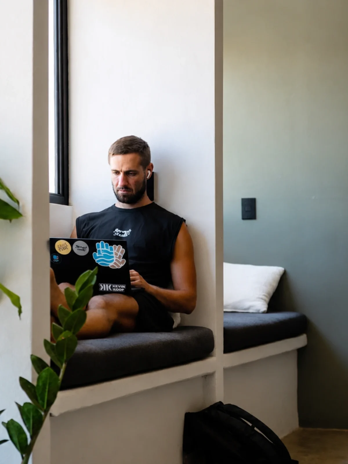 Man working on a laptop while seated in a built-in window nook surrounded by indoor plants